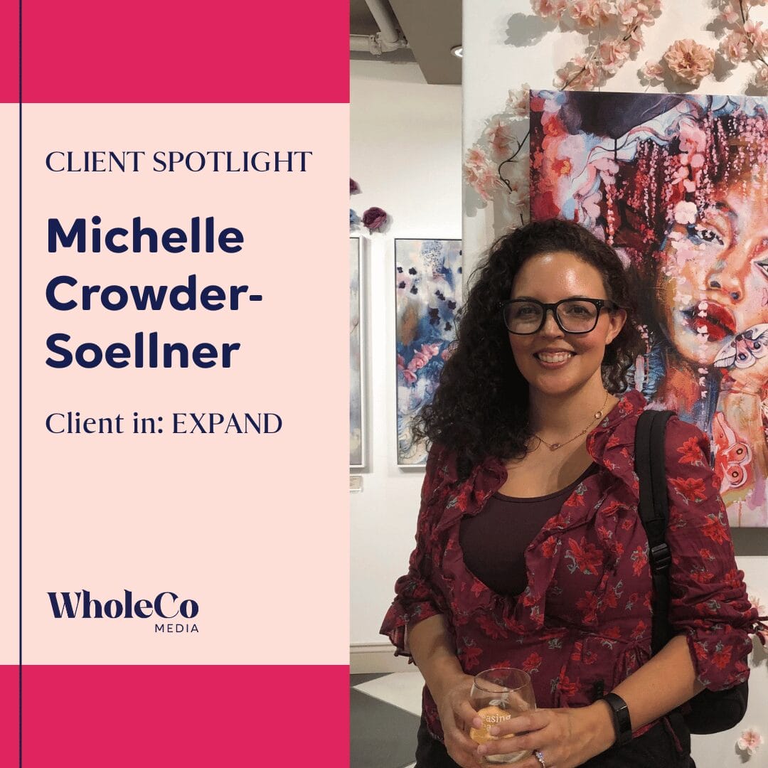 Photo of Michelle, who has black curly hair, glasses, and a big smile standing against a backdrop of phenomenal art.